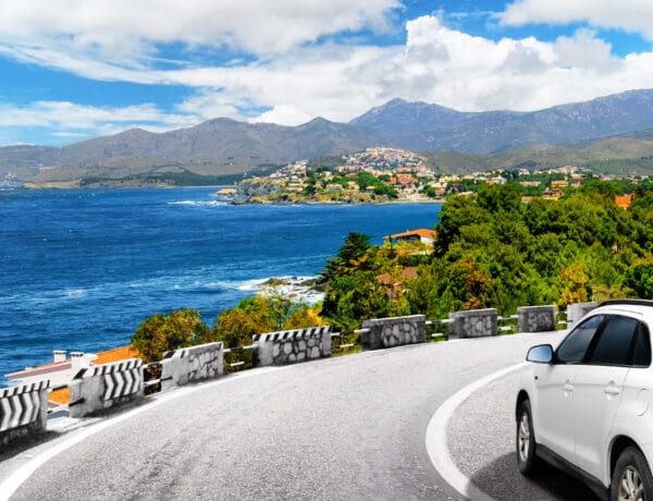 A white car drives by the road in mountains to the sea.